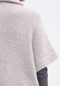 Poncho tricoté gris clair avec des manches courtes, un motif texturé et des accents côtelés sur les bords. Matière douce et confortable.
