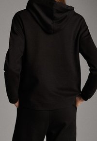 Mustat hupparit, joissa on teksturoitu pinta, pitkät hihnat ja leveä vyötärönauha, nähtynä takaa.