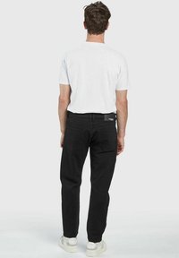 Svarta denimbyxor med rak skärning, prydda med bakfickor och en tygmärkning. Kombinerat med en enkel vit t-shirt och vita sneakers.