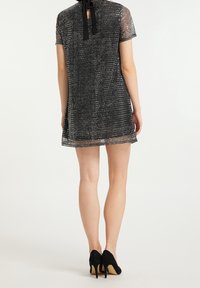 Svart, genomskinlig klänning med korta ärmar och hög halsringning. Har ett texturerat mönster och ett svart band knutet bak på klänningen.