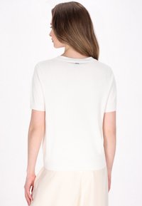 Hvid kortærmet strikket sweater, let materiale, ribbet halsudskæring og kant, med en afslappet pasform. Enkelt design, ingen mønstre eller udsmykninger.