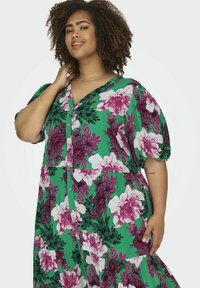 Grünes Blumenkleid mit großen rosa und weißen Blumen, kurzen Puffärmeln, einer durchgehenden Knopfleiste und lockerer Passform.