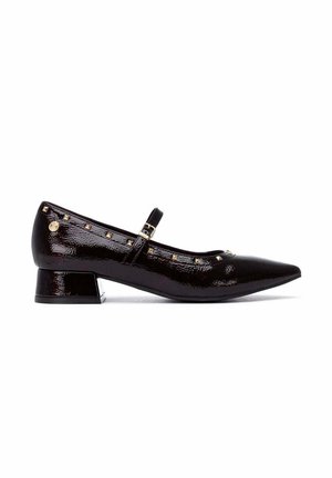 Zapato de charol negro con tacón bajo, puntera puntiaguda, correa en el tobillo con hebilla y pequeños remaches dorados a lo largo del borde superior.