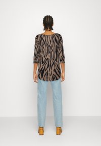 Langarmshirt mit einem braun-schwarzen Zebra-Strich-Muster. Weicher Stoff, runder Ausschnitt und verlängerte Rückseite. Kombiniert mit hellblauen Jeans.