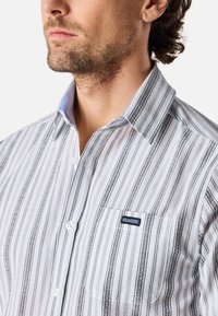 Camicia con bottoni, a strisce verticali blu, bianche e grigie. Presenta una tasca sul petto con il logo "SEASIDE", colletto a punta e una texture di tessuto liscia.