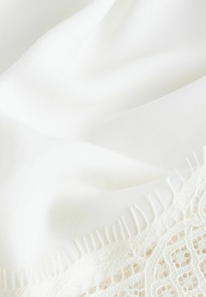 Fehér szövet sima textúrával, csipkedíszítéssel a szélén és vékony rojttal, amely a lágy eleganciát és a finom mintákat ötvözi.