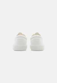 White canvas sneakers with textured rubber soles, rounded backs, and subtle stitching details, featuring a minimalistic design.