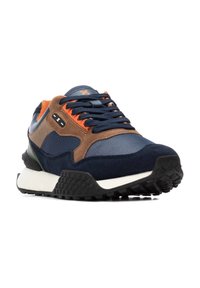 Zapatilla atlética en navy y marrón, con materiales de malla y ante, acentos naranjas, suela negra texturizada y elementos de diseño de múltiples capas.