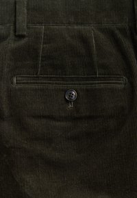 Pantalon en velours côtelé marron avec nervures verticales, doté d'une poche arrière unique et d'une fermeture à bouton noir.