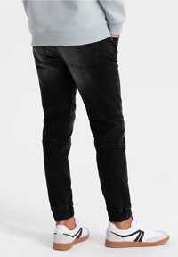 Svarta tapered jogger-byxor i denim med elastiska muddar, med flera sömmar och en blekt tvätt, kombinerat med vita sneakers och grå sweatshirt.