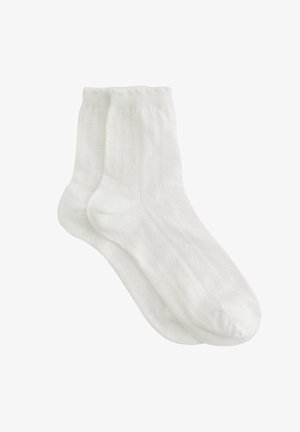 Valged puuvillased sokid soonilise tekstuuri ja väikeste mustritega. Neil on keskmise pikkusega varreosa ning ülaosas sile ja elastne äär.