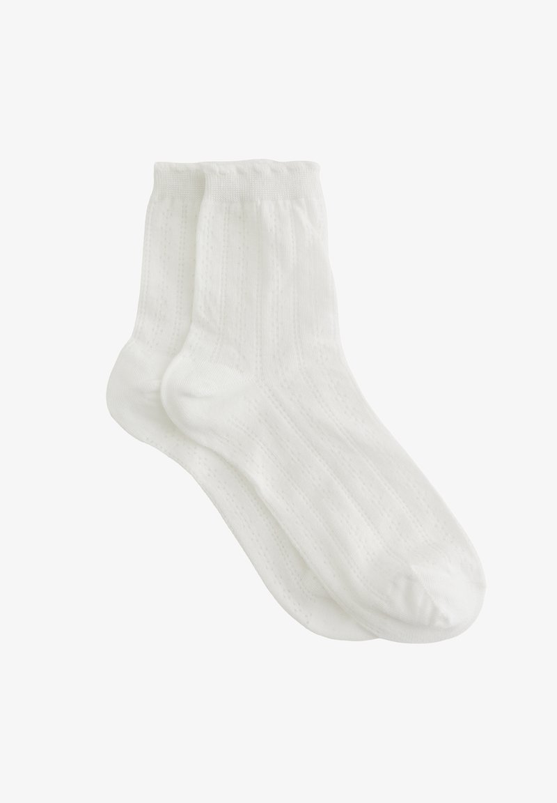 Chaussettes blanches en coton avec une texture côtelée et de petits motifs. Elles ont une longueur mi-mollet et une bordure élastique lisse en haut.