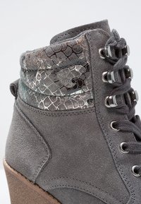Bottine en daim gris avec texture métallisée effet peau de serpent sur le col, fermeture à lacets, œillets métalliques et talon compensé.