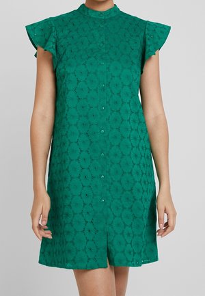 Vestido verde abotonado con patrón floral calado y mangas cortas acampanadas, llevado por una persona sobre un fondo liso.