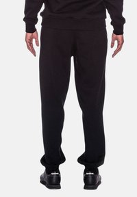 Schwarze Sweatpants mit einer entspannten Passform, aus weichem Material gefertigt. Rippbündchen und Bund, mit Taschen an den Seiten. Schwarze Sneaker getragen.