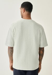 Short-sleeve, crew-neck shirt in light gray with a textured, woven pattern. Features a relaxed fit and a straight hem, displayed from the back.