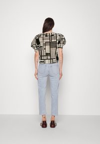 Blusa con estampado negro y crema, con mangas abullonadas, combinada con jeans de mezclilla azul claros. La blusa presenta diseños geométricos y un corte holgado.
