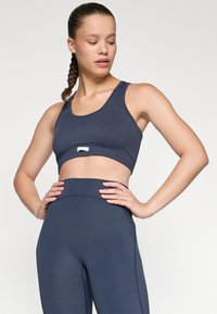 Top corto deportivo color azul marino con una banda ancha, textura suave y un mínimo de marcas; combinado con leggings de tiro alto a juego.