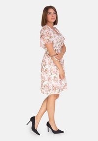Floral Kleid mit kurzen, schwingenden Ärmeln in Hellrosa und Weiß, ausgestattet mit einer taillierten Taille und einem fließenden Rock. Kombiniert mit schwarzen Stilettos.
