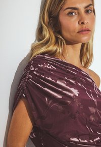 Burgundia kleit tekstuuriga lillemustriga, kokku korjatud detailiga ühel õlal, valminud sileda, satiinitaolise kangaga.