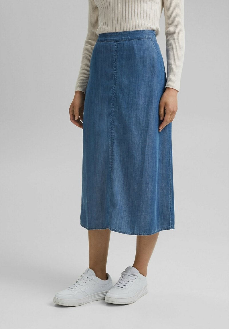 Jeanskjol i midilängd i ljusblå ton, med slät textur, elastisk midjeresår och sidseamsdetaljer, kombinerad med vita sneakers.