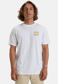 White cotton t-shirt featuring a small yellow and blue logo patch on the left chest area. Classic crew neck and short sleeves.