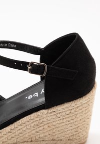 Schwarze Wildleder-Wedge-Sandale mit Espadrille-Seilsohle, verstellbarem Riemen mit silberner Schnalle, glattem Innenfutter und flachem schwarzem Fußbett.