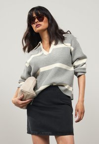 Gray striped pullover sweater with a V-neck, paired with a black denim skirt. The model holds a beige textured clutch bag.