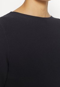 Pull en maille bleu marine avec une texture côtelée, doté d'un col rond et d'une coupe décontractée. Vue en gros plan mettant en valeur les détails du matériau.