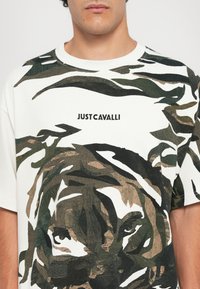 White t-shirt featuring a green, brown, and black tiger graphic, with "JUST CAVALLI" text beneath the design. Short sleeves, crew neckline.