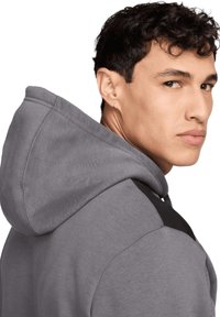 Felpa grigia con cappuccio regolabile e un accentuazione nera sulla spalla. Realizzata in tessuto morbido, presenta una finitura testurizzata e un cappuccio avvolgente.