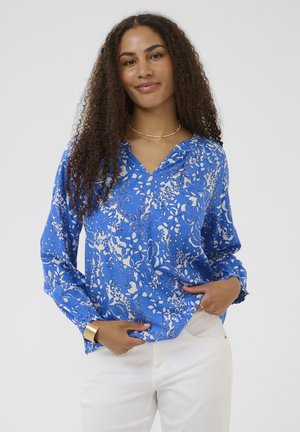 Modrá kvetinová blúzka s dlhými rukávmi, výstrihom do V a nariasenými detailmi. Vyrobená z hladkej látky s bielymi kvetinovými vzormi.