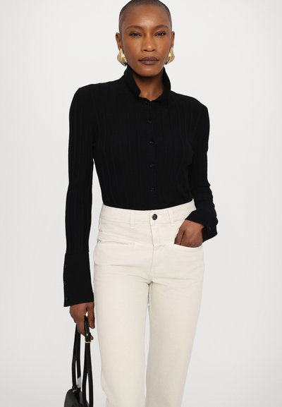 Black ribbed long-sleeve blouse with a collared neck and button-down front, paired with off-white high-waisted pants and a black handbag.
