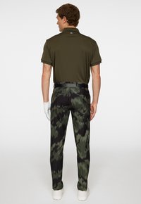 Herrarnas olivgrön pikétröja som matchas med svarta och gröna kamouflagebyxor, med en stilren design och ett svart bälte. Vit handskaccent.