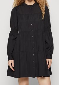 Black button-down dress with long puff sleeves, gathered bodice, and tiered skirt. Made of smooth fabric, featuring a classic collar and discreet buttons.