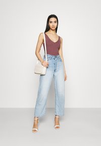 Geribbelde bordeaux mouwloze top gecombineerd met lichtblauwe rechte spijkerbroek en witte sandalen met banden. Kleine beige crossbody tas met een gewatteerd ontwerp.