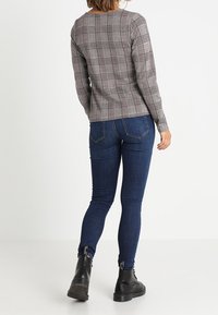 Haut à manches longues à carreaux gris et rouges avec un col rond, associé à un jean bleu foncé ajusté et des bottines noires.