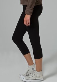 Zwarte cropped leggings van rekbaar materiaal, gecombineerd met lichtgrijze hoge sneakers met zwarte accenten.