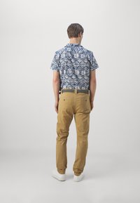 Cămașă cu mânecă scurtă cu un model geometric albastru și alb, asortată cu pantaloni chinos crem din bumbac și adidași albi.