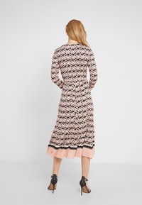 Šaty s vzorem a dlouhými rukávy, které mají kombinaci černých, růžových a bílých tvarů. Spodní lem má volánkovou růžovou vrstvu a černé akcenty.