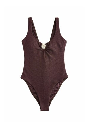 Braunes, strukturiertes Kleid mit tiefem Ausschnitt, das durch eine runde goldene Schließe mit einem stilisierten Buchstaben „b“ in der Mitte der Brust zusammengehalten wird.