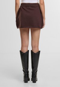 Weinroter Strickrock mit einem taillierten Bund, kniehohem Schnitt und subtiler Textur; kombiniert mit schwarzen kniehohen Stiefeln mit Absatz.