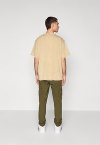 Beige oversized t-shirt with a textured finish, paired with green cargo pants featuring side pockets, and white sneakers.