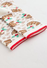 Calze al ginocchio in maglia bianca, con stampa leopardata beige, motivo di dolce di Natale, dettagli rossi in cima e foglie di agrifoglio verdi.