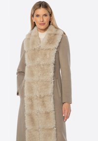 Lange beige jas met een zachte, vachtachtige voorkant. Heeft rechte mouwen en zijzakken; zachte textuur en op maat gemaakt ontwerp.