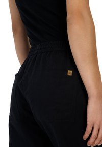 Zwarte broek met een elastische tailleband, met twee achterzakken en een klein merketiket. De stof lijkt zacht en duurzaam te zijn.