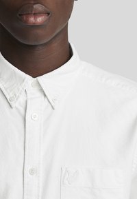 Witte button-up shirt gemaakt van katoen, met een klein geborduurd logo op de linkerkant van de borstzak en een opstaande kraag.