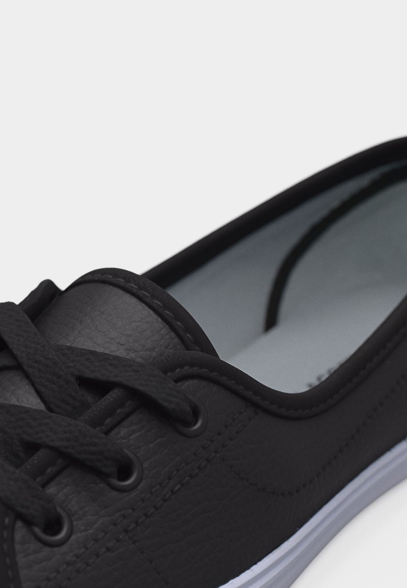 Schwarzer Sneaker mit niedrigem Schaft, strukturierter Lederfront, schwarzen Schnürsenkeln und weißer Gummisohle, aus nächster Nähe aufgenommen.