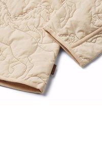 Vadderad filt i ljusbeige med hästbroderi. Har en strukturerad yta och dekorativ kant. Tag synlig i hörnet.