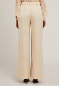 Vida byxa i krämfärgad satin med en slät yta, skräddarsydd midja och en lös passform som faller ner till golvet.